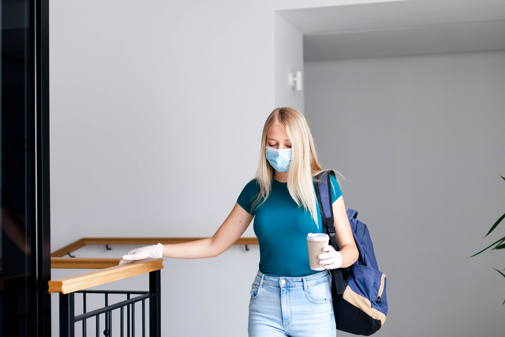 Female student in mask indoors going to exams in high school. woman in empty university. Girl with backpack and book in college corridor during quarantine.